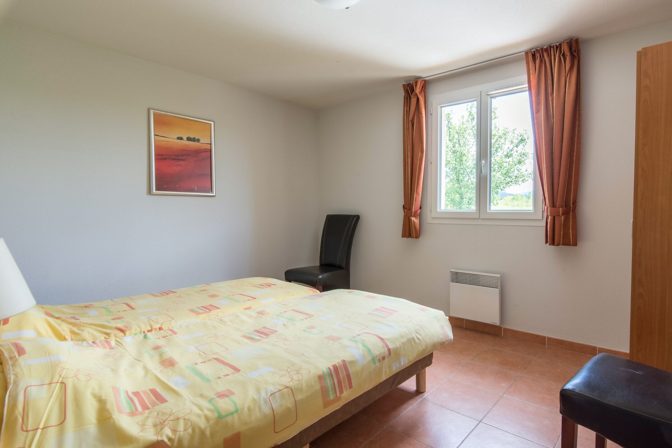 A bedroom with a bed, a chair, a radiator, and a window with curtains.