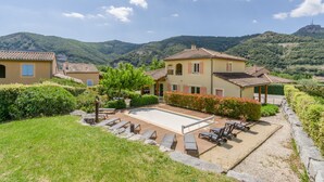 Une villa avec piscine, des chaises longues et une vue sur des collines verdoyantes.