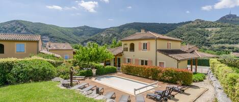 A villa with a swimming pool, lounge chairs, and a view of green hills.