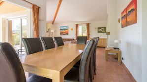 Un espace repas avec une longue table en bois, des chaises en cuir noir et une vue sur l’extérieur grâce à de grandes fenêtres.