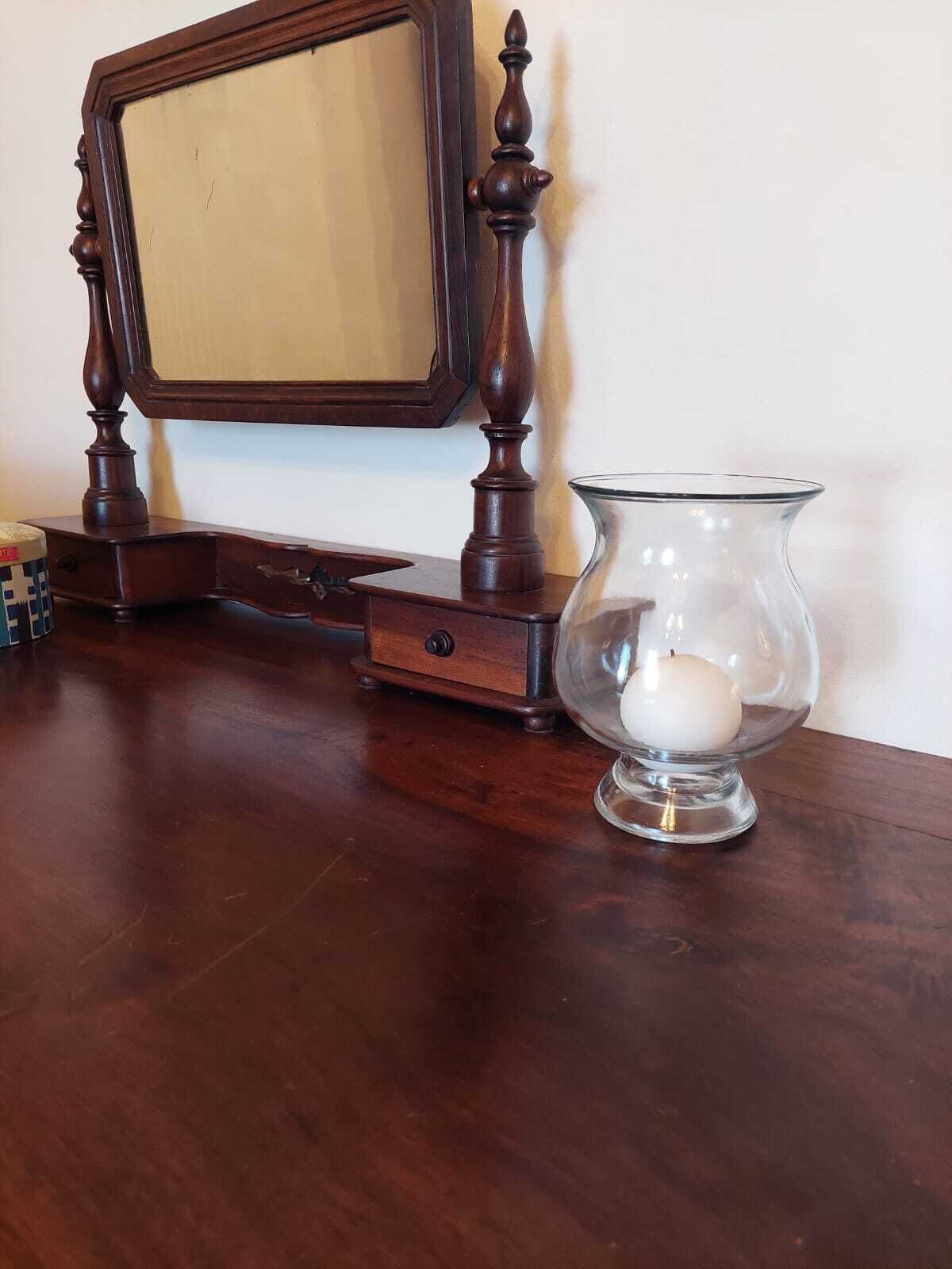 Un tavolo di legno con uno specchio, un portacandele in vetro e un piccolo contenitore.