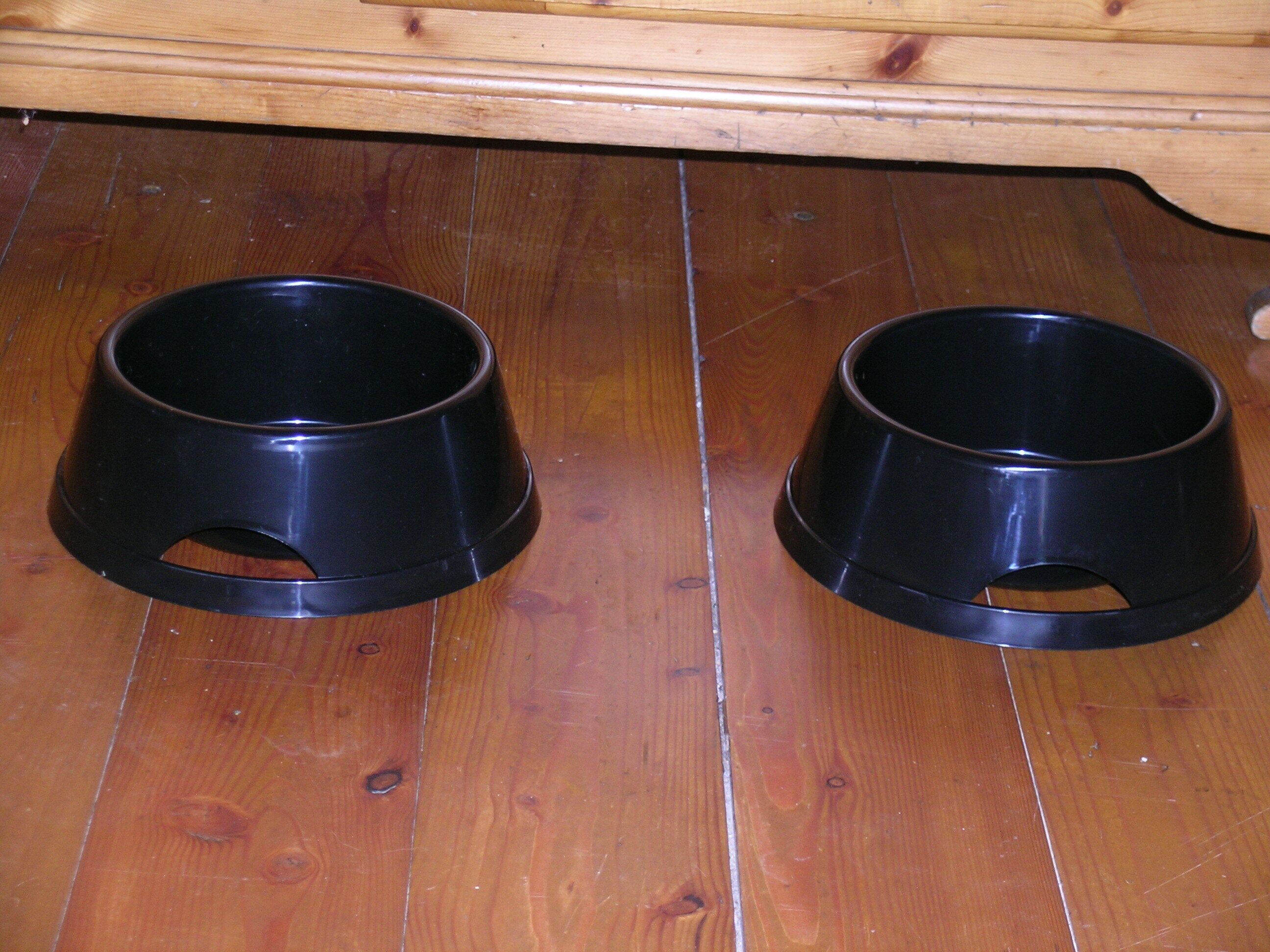 Zwei schwarze Futternäpfe auf einem Holzboden.