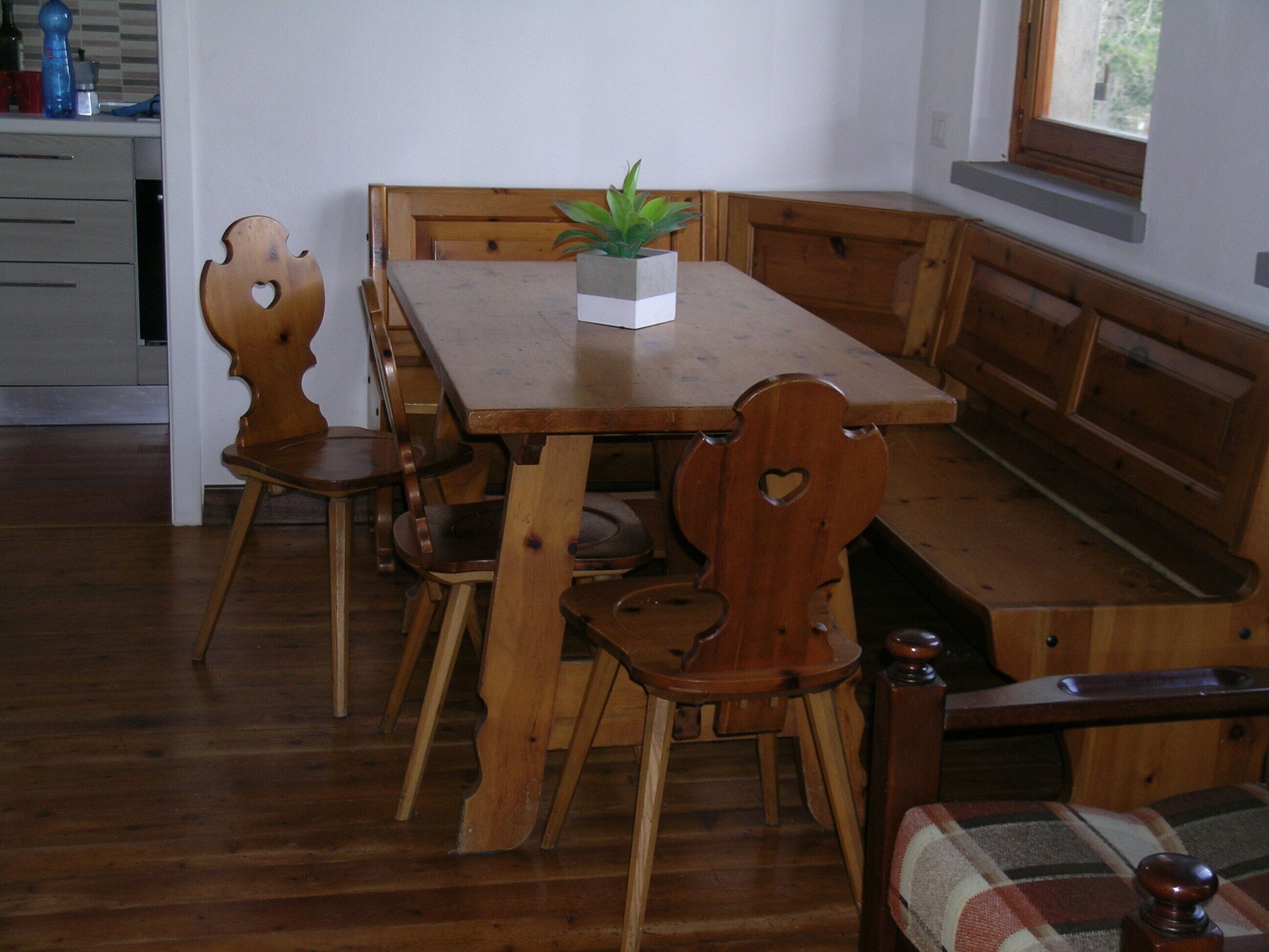 A wooden dining table with bench seating, a potted plant, and a window with a view.