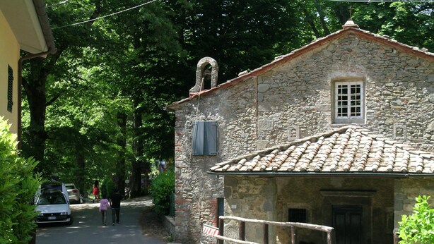 Une rue étroite bordée d’un bâtiment en pierre, doté d’un toit recouvert de tuiles et d’une petite fenêtre.