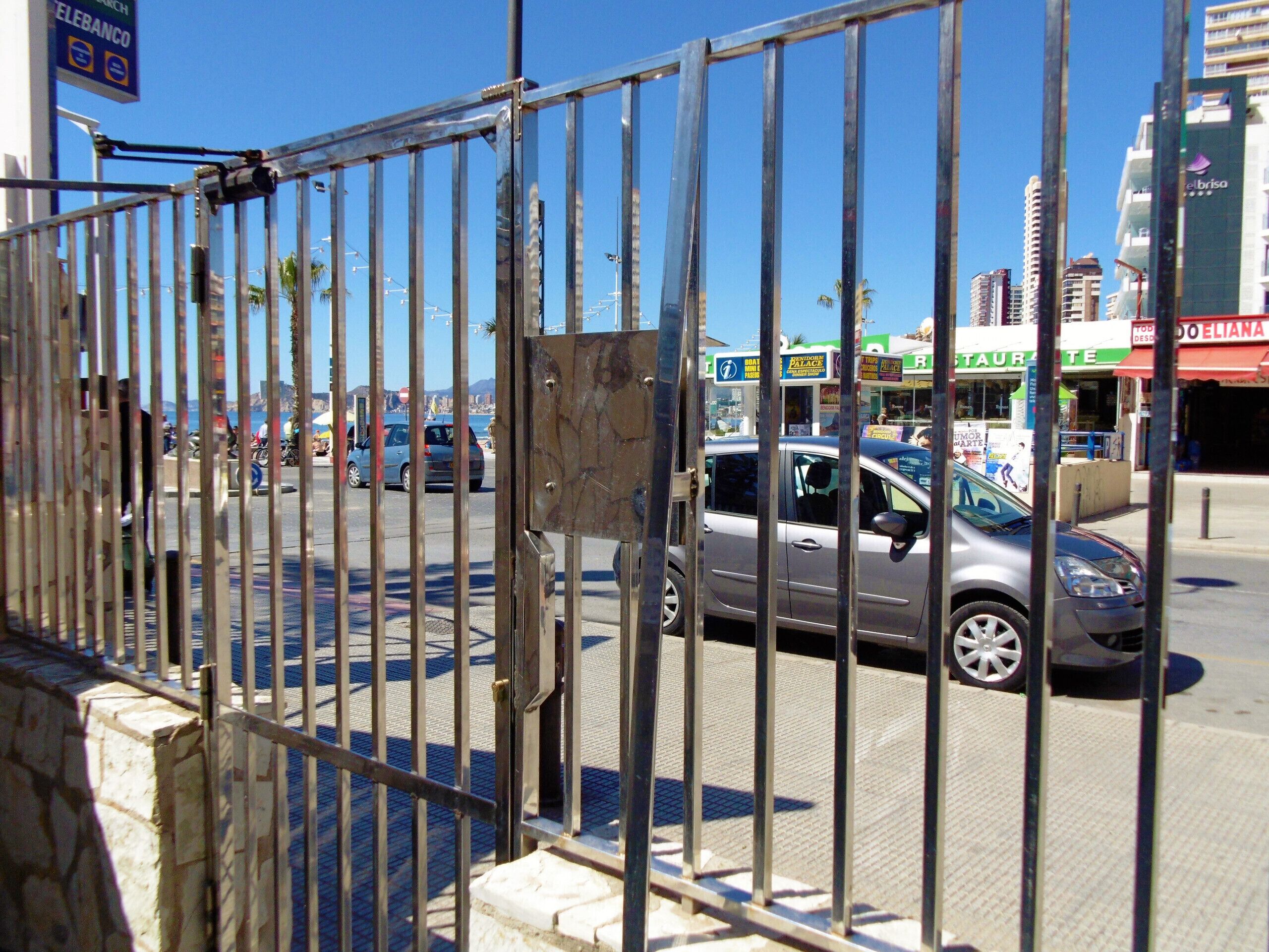 A street view with a metal fence, cars, and buildings including a restaurant and a bank.