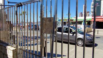 A street view with a metal fence, cars, and buildings including a restaurant and a bank.