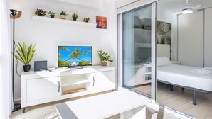 A modern living room with a flat-screen TV, white furniture, a glass door leading to a balcony, and a ceiling fan. - Carabelas III 1-3 (Benidorm)