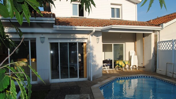 A residential property with a swimming pool, a covered patio, and a sliding glass door leading to an interior space.