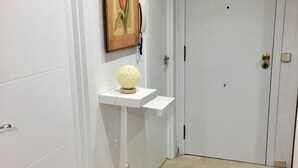 Un pasillo con paredes blancas, una puerta, un estante pequeño con un objeto decorativo y un cuadro.