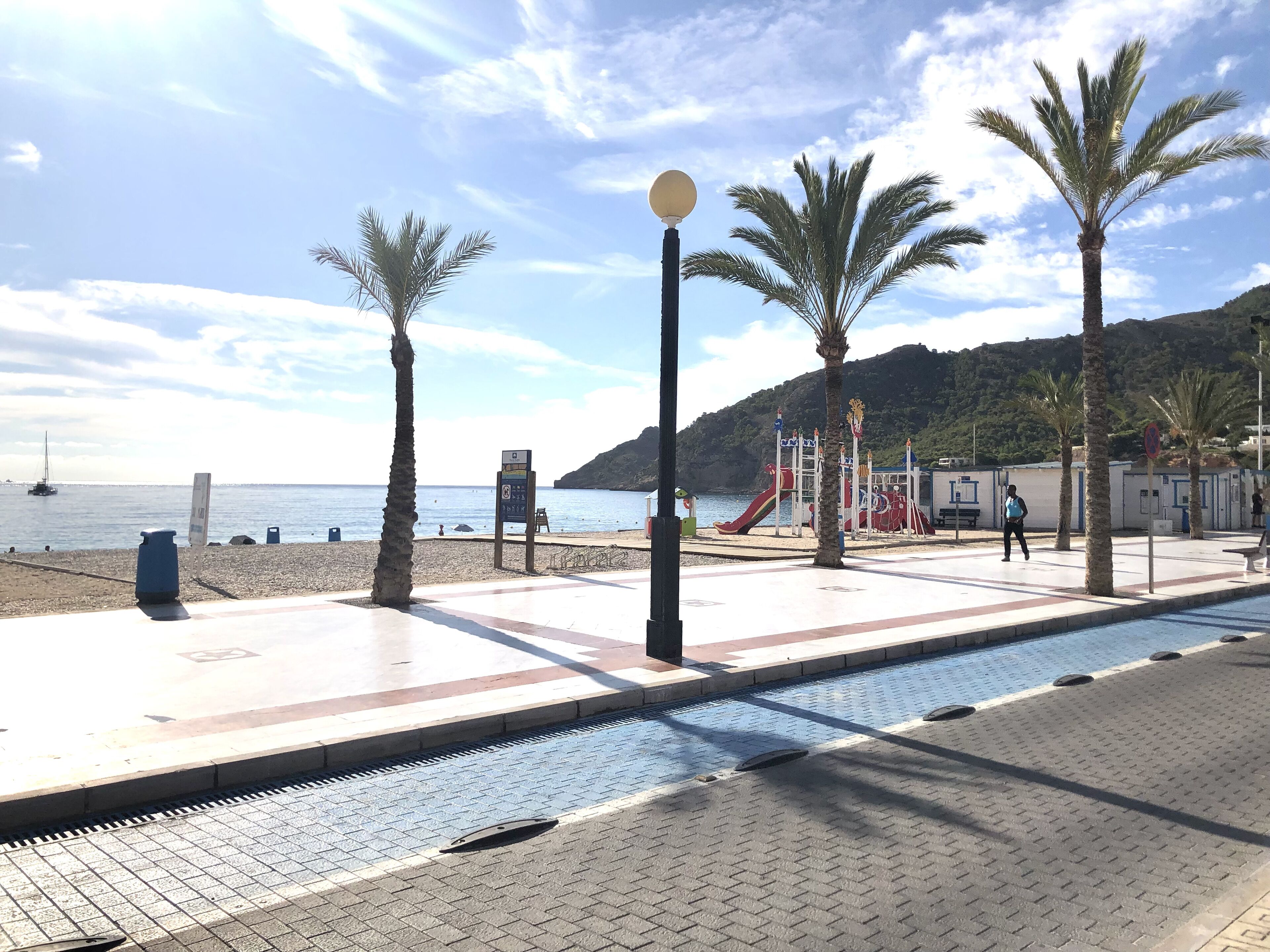 A beachside walkway with palm trees, a playground, and a view of the sea.