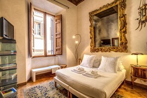 A bedroom with a large bed, a wooden bench, a bedside table, a mirror, and a bookshelf.