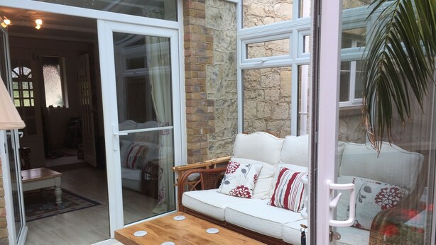 A cozy room with a wooden table, a white sofa with patterned cushions, and a stone wall. - Edge of Old Village, close to shops, park and beach; ferry discounts (Shanklin)
