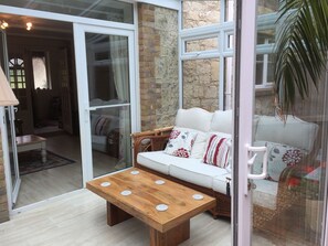 A cozy room with a wooden table, a white sofa with patterned cushions, and a stone wall. - Edge of Old Village, close to shops, park and beach; ferry discounts (Shanklin)