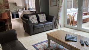 A living room with a sofa, a coffee table, and a view of the kitchen and outdoor seating area. - Edge of Old Village, close to shops, park and beach; ferry discounts (Shanklin)