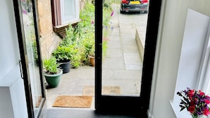 A narrow entrance with a glass door leading to a small outdoor area with potted plants and a view of parked cars. - Central Apartment Linlithgow, near Edinburgh (Linlithgow)