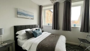 A modern bedroom with a large bed, a nightstand, a lamp, a painting, and a window with curtains. - Central Apartment Linlithgow, near Edinburgh (Linlithgow)