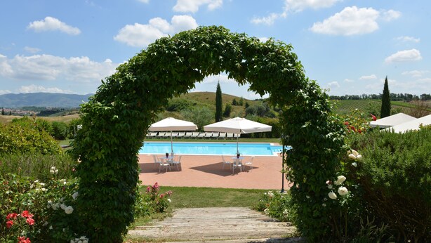 Un área de piscina con un sendero de madera que conduce a sombrillas y sillas blancas.