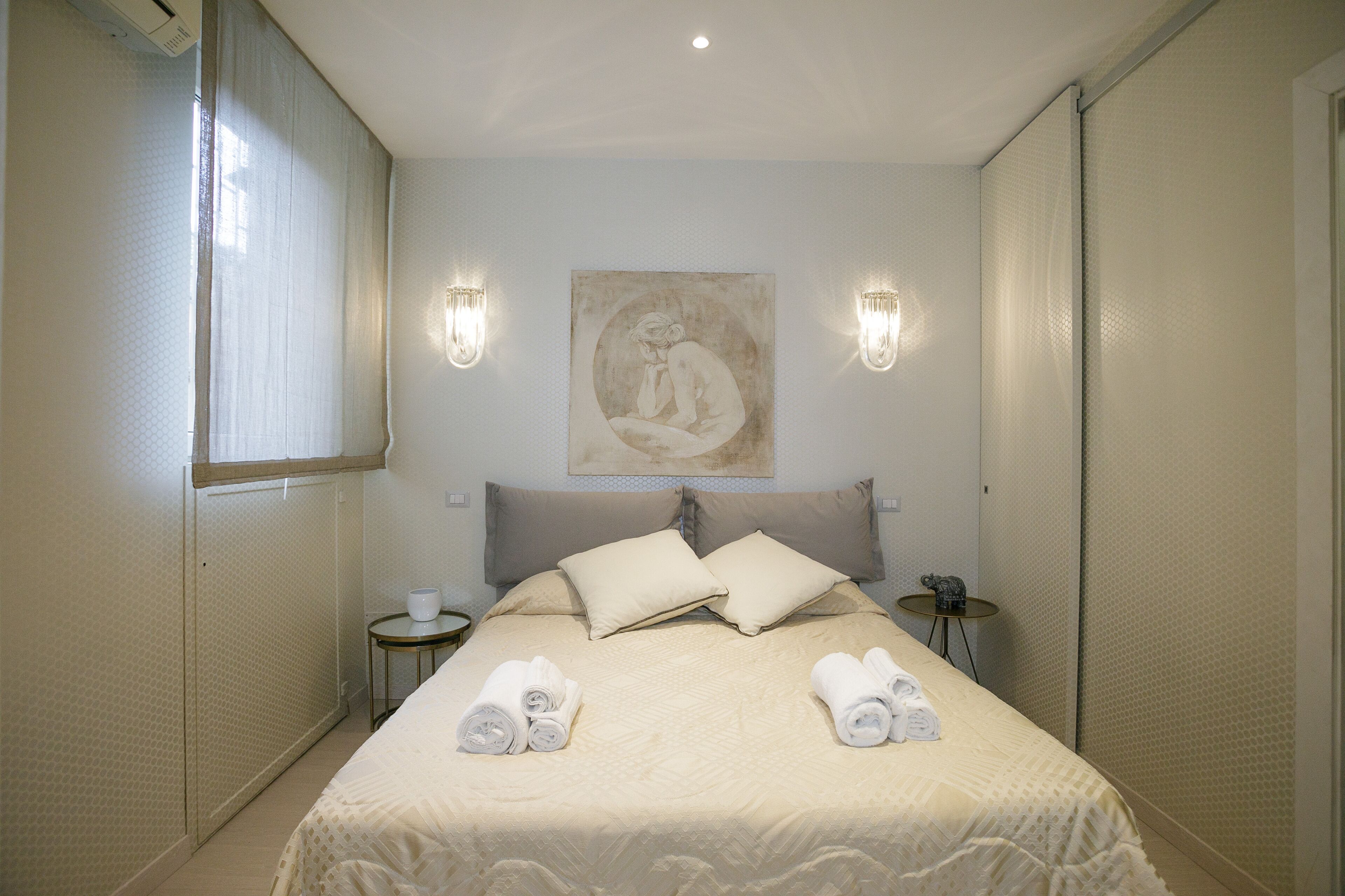 A hotel room with a bed, two bedside tables, a wall-mounted artwork, and a window with curtains.