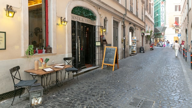 Eine Kopfsteinpflasterstraße mit Außenbestuhlung eines Restaurants namens 'Antica Osteria'.