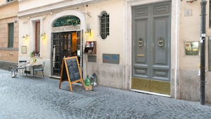 Eine Kopfsteinpflasterstraße mit einem Restaurant namens „ANTICA OSTERIA“, das Außenplätze und eine Kreidetafel mit der Speisekarte bietet.