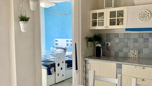 A modern kitchen with white cabinets, a glass-top table, and hanging plants.