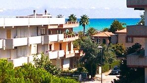 A multi-story residential building with balconies, a street view, and a clear view of the sea.