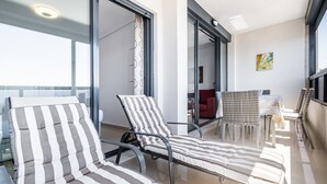 Un balcón con sillones reclinables a rayas, una mesa de vidrio y un sofá rojo.