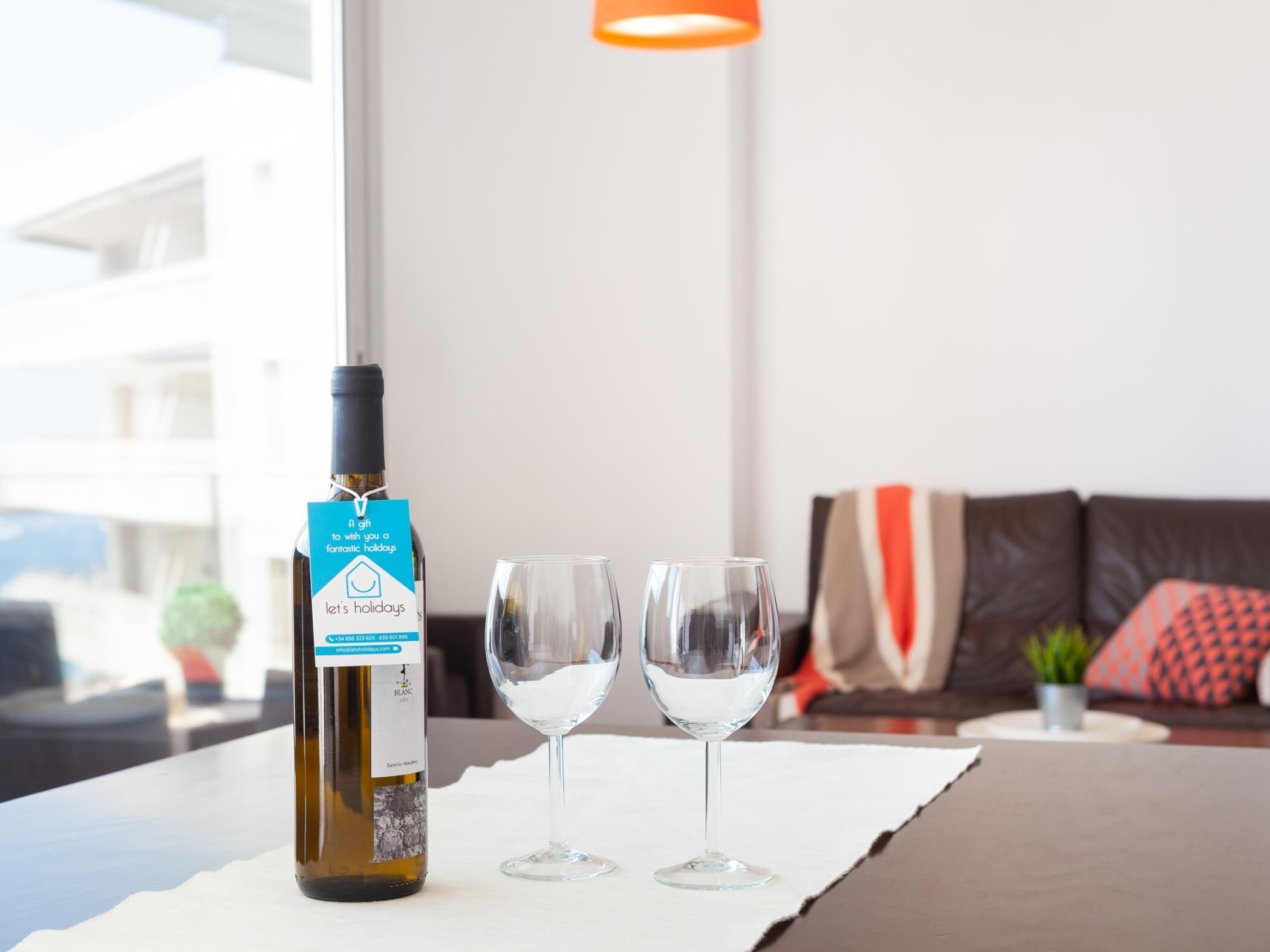 A bottle of wine with a label, two empty wine glasses, and a table in a room with a view.