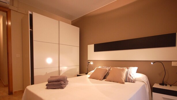 Une chambre moderne avec un grand lit, une armoire et une table de chevet avec une lampe.