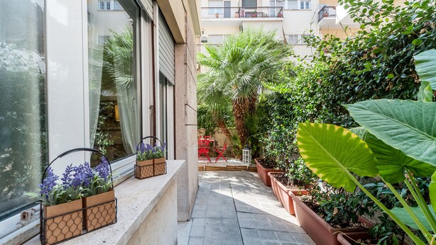 Passatge exterior estret amb plantes en testos i una cadira vermella.