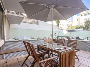 An outdoor patio with a wooden table and chairs, a large umbrella, and a view of buildings in the background. - Loft near the Sagrada Familia 6 pax Pool & Terrace -WiFi free (Barcelona)