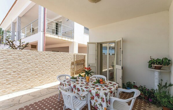 Une terrasse extérieure avec une table dressée pour le repas, entourée de chaises blanches et agrémentée de diverses plantes en pot.