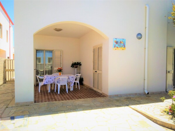 A covered patio with a table and chairs, a potted plant, and a wall-mounted sign.