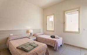 Une chambre d’hôtel avec deux lits, une table de chevet avec une lampe et deux fenêtres.