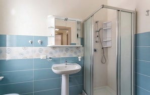 A bathroom with a glass shower enclosure, a pedestal sink, and a mirror above it.