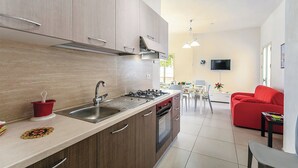 Een moderne keuken met een spoelbak, fornuis en kasten, een zithoek met een rode bank en tafel, en een televisie aan de muur.