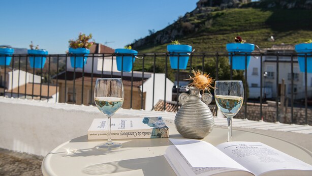 A table with two wine glasses, a book, and a vase with a decorative item. - Casilla Daleá, Andalusia center, Natural Park, by Planetrural (Carcabuey)