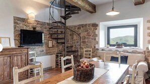Un interior rústico con pared de piedra, muebles de madera, una escalera de caracol y un amplio ventanal con vistas.