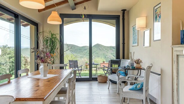 Un comedor con mesa de madera, sillas blancas y vistas a las colinas.