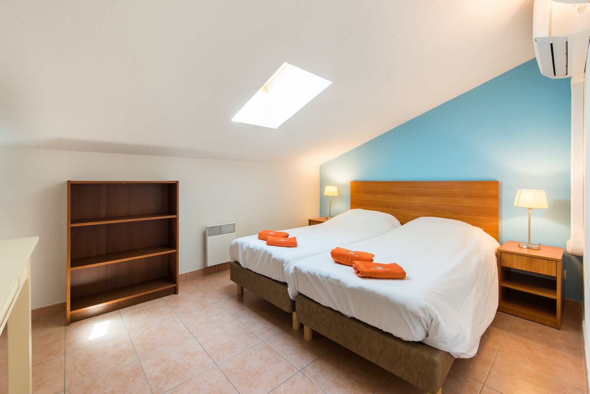 Une chambre avec deux lits, une armoire en bois, un radiateur et un luminaire au plafond.