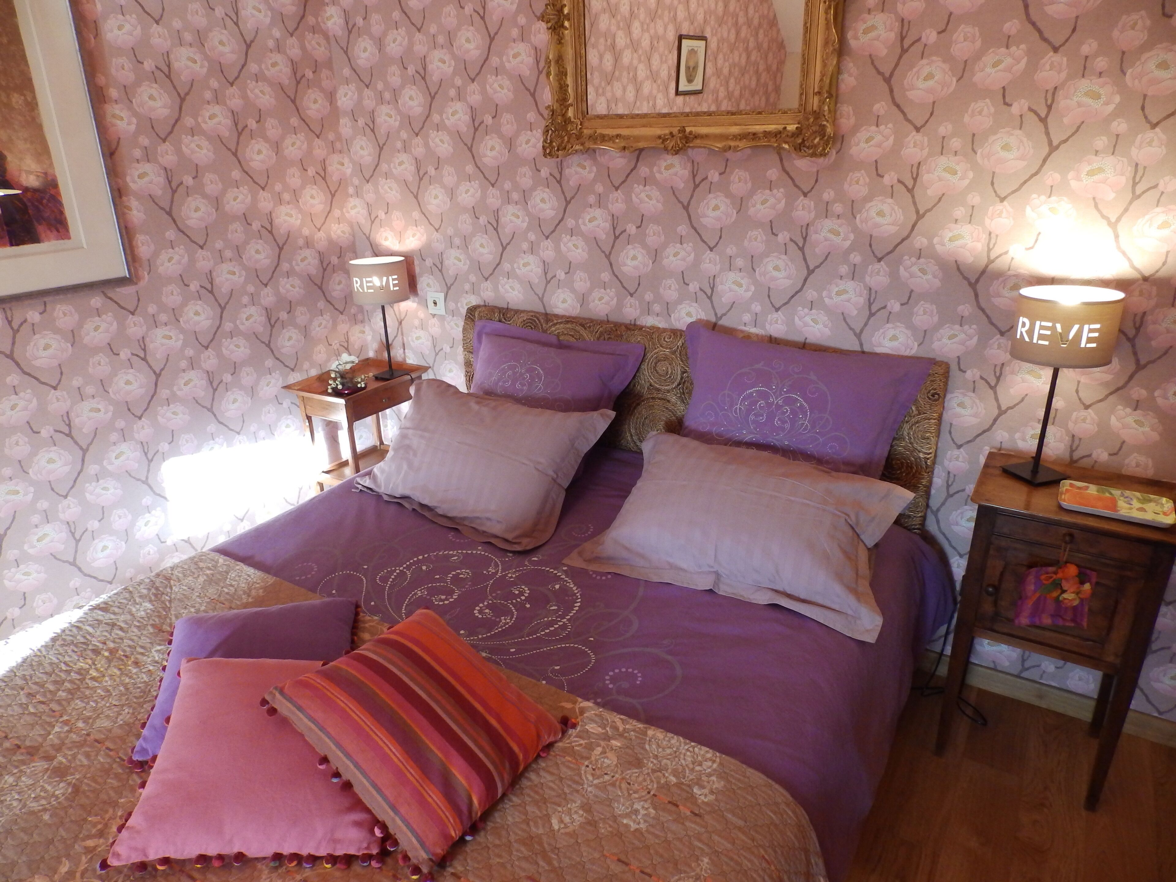 A bedroom with a bed, pillows, a nightstand, a lamp, and a wall with floral wallpaper.
