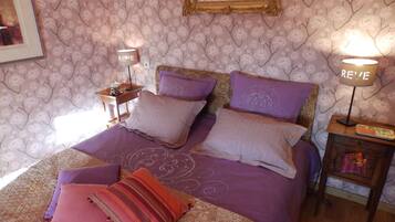 A bedroom with a bed, pillows, a nightstand, a lamp, and a wall with floral wallpaper.