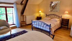 A bedroom with a bed, two bedside tables with lamps, a chair, a radiator, and a window with curtains.
