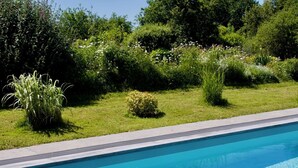 A swimming pool with a clear blue water surface, surrounded by lush green grass and various shrubs.