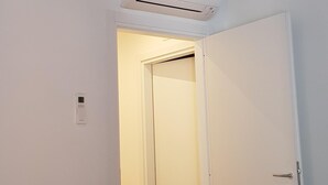 A room with a wooden ceiling, an air conditioning unit, a white door, and a stack of white towels on the floor.
