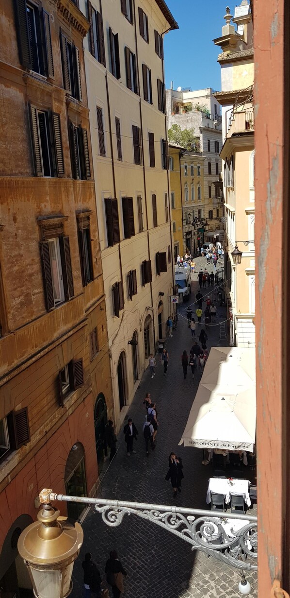 A narrow street with buildings on either side, a cobblestone surface, and people walking.