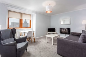 Een moderne woonkamer met een grijze bank, een grijze fauteuil, een witte salontafel en een televisie op een dressoir.