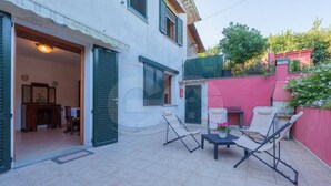 Une cour avec une table à manger et des chaises, une petite table sur laquelle est posé un vase, et une porte donnant sur un espace intérieur.