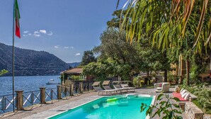 Ein Poolbereich mit Liegestühlen, einem kleinen Pool und Blick auf einen See mit Bergen im Hintergrund.