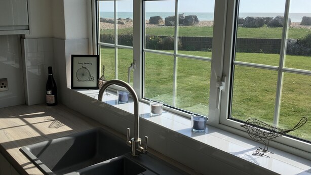 A kitchen with a double sink, a wine bottle, and a framed picture of a bicycle. - Stunning Beachfront Apartment on Ferring beach (Ferring)